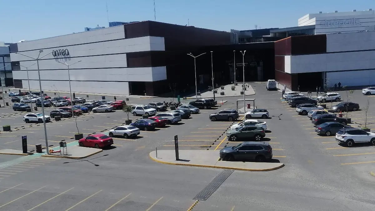 Outdoor parking lot filled with various vehicles in front of a large industrial warehouse building with horizontal striped exterior