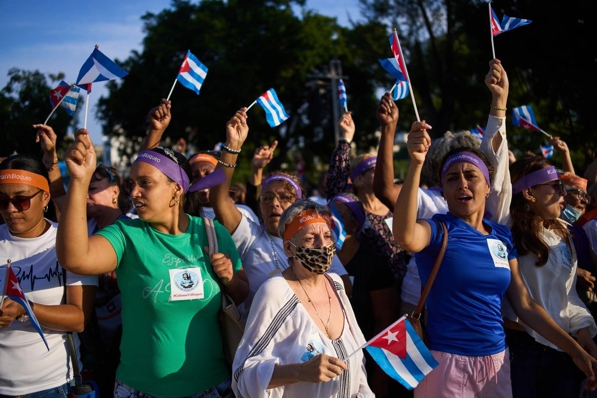 Crowd of people holding Cuban flags aloft at an outdoor political rally or demonstration with trees in background