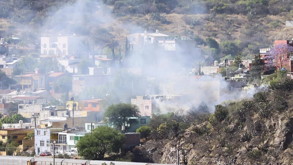 Dense smoke billows from a hillside residential area with multi-story buildings scattered across the terrain