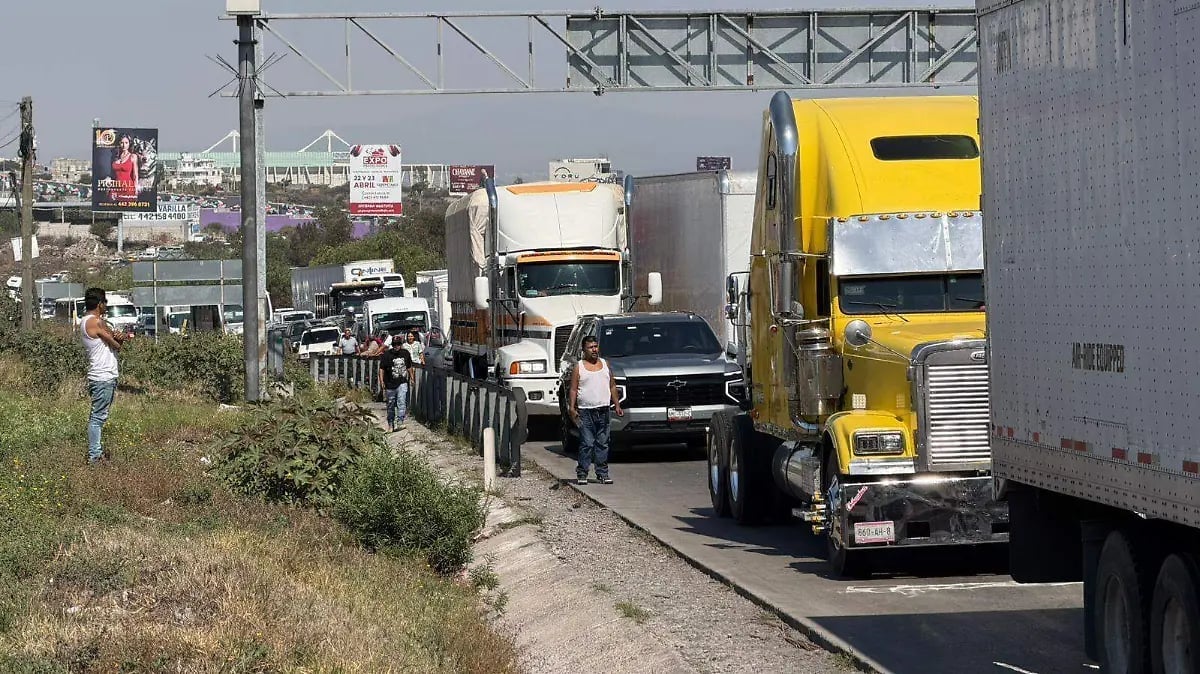 Multiple commercial trucks lined up on a congested roadside with power lines and buildings in the background