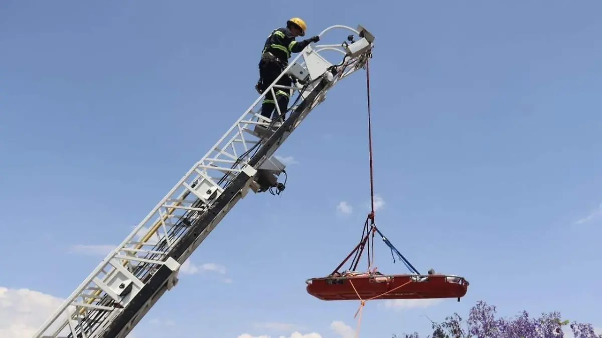 Firefighter operating an aerial ladder truck with a red rescue basket suspended by cables against a blue sky