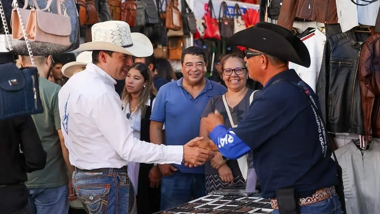Group of people at an indoor market or event, with two men in cowboy hats shaking hands while others look on