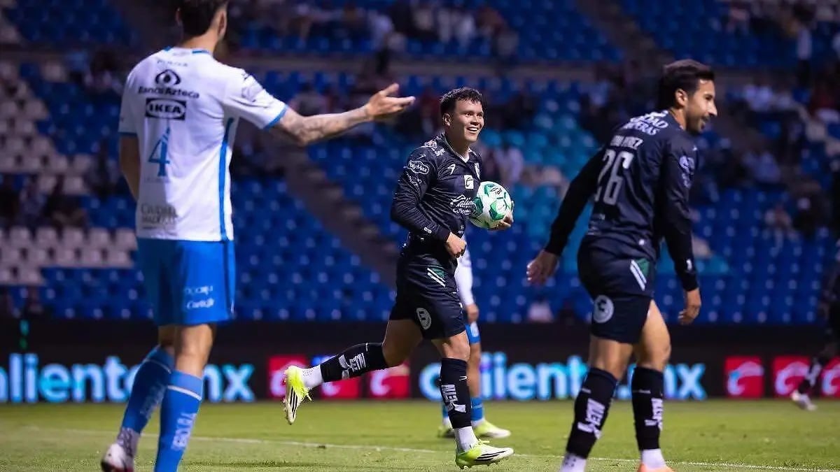 Soccer players during a match, one in white and blue jersey gesturing, others in black uniforms on the field at night