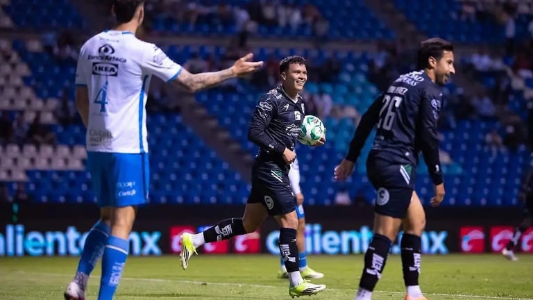 Soccer players during a match, one in white and blue jersey gesturing, others in black uniforms on the field at night