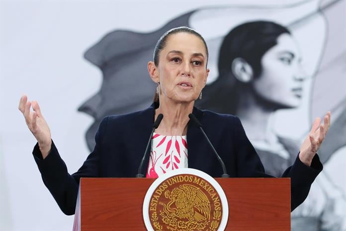 Woman speaking at podium with Mexican presidential seal, gesturing with hands during official press conference