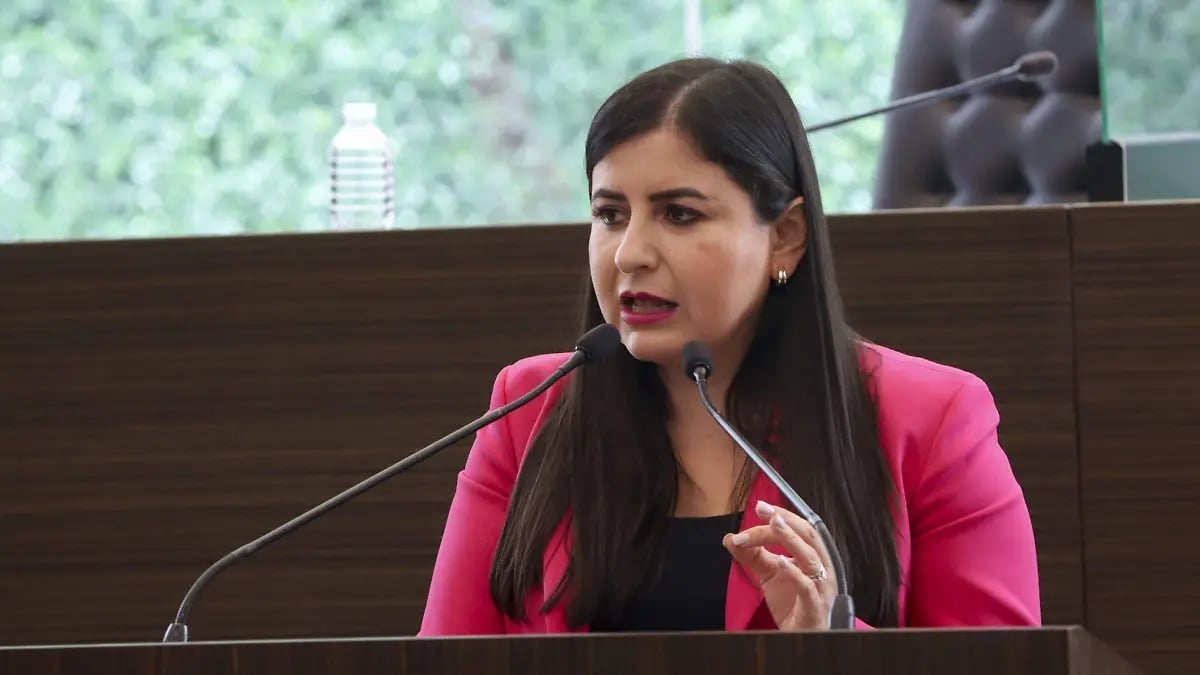 Woman in hot pink blazer speaking at microphone during formal presentation or meeting