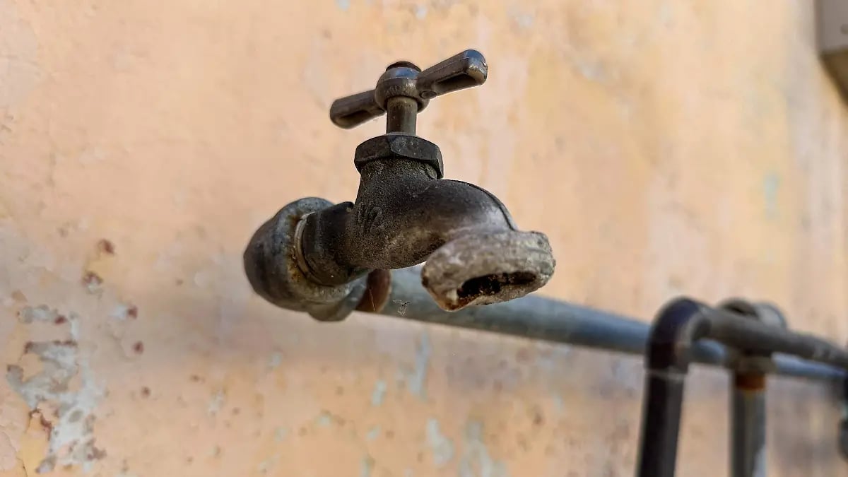 Close-up of an old, rusty outdoor water faucet mounted on a weathered beige wall