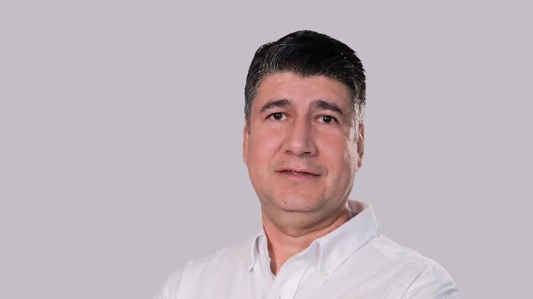 Middle-aged man with dark hair wearing a white shirt, posing against a light gray background